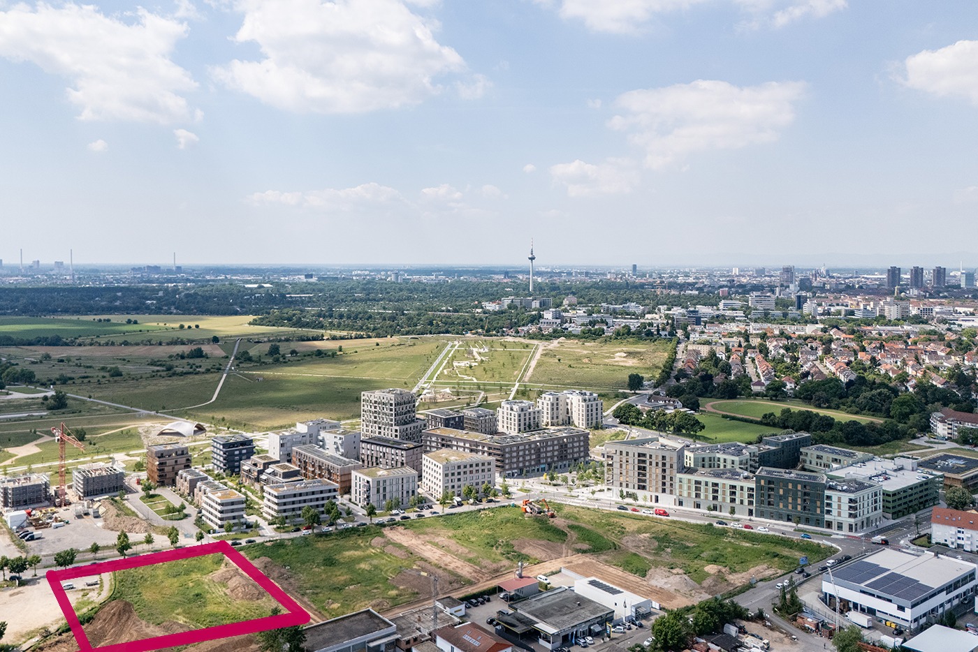 KI-basierte Bildbeschreibung | Luftaufnahme des SPINELLI Quartiers mit modernen Wohn- und Geschäftsgebäuden, offenen Grünflächen und einer rot umrandeten Brachfläche im Vordergrund.