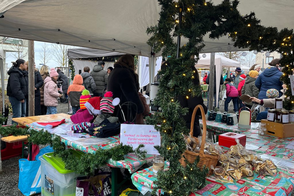 KI-basierte Bildbeschreibung | Marktszene im Freien mit einem weihnachtlich geschmückten Stand, an dem Backwaren und Hüte verkauft werden, Menschen in Winterkleidung, die sich umsehen, und festliche Dekorationen.